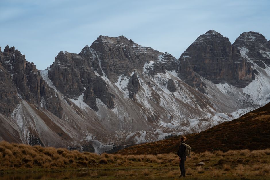 Hiker admiring a stunning snowy mountain range under a clear sky.