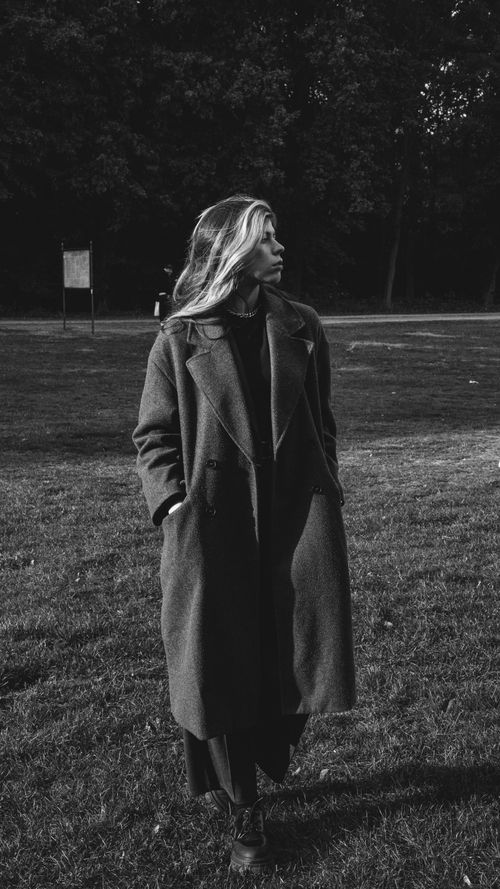 Free Black and white photo of a woman in a coat walking in a park, exuding elegance. Stock Photo