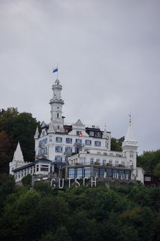 Majestic Château Gütsch overlooking Lucerne, surrounded by lush greenery and a cloudy sky.
