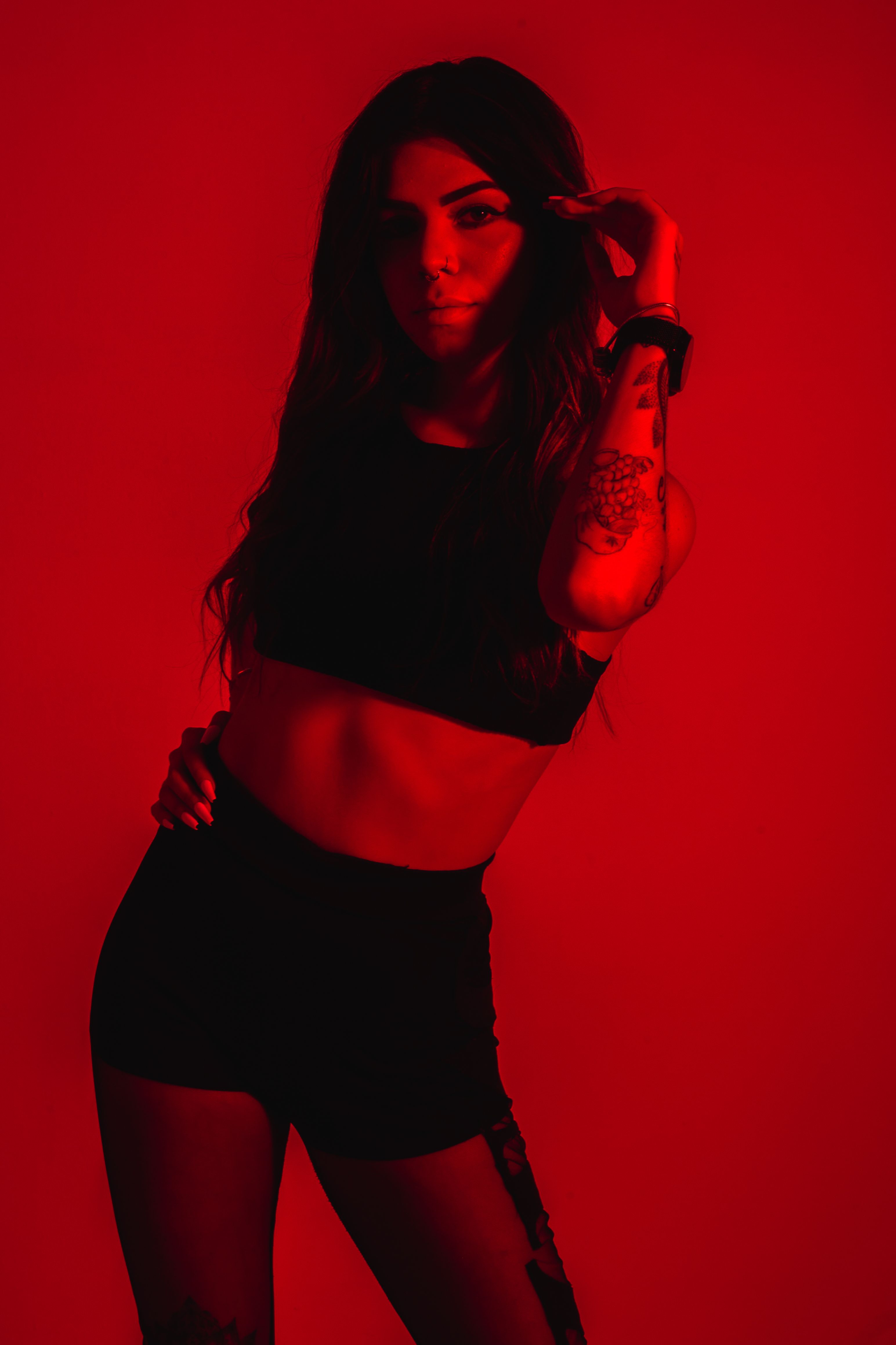 Fashionable woman poses in red lighting during studio shoot, displaying modern style.