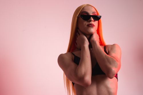 Free Stylish woman with long hair and sunglasses posing confidently in a studio with a pink background. Stock Photo