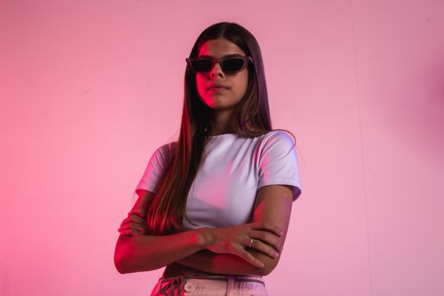 Free Confident young woman in sunglasses posing against a pink background in a studio setting. Stock Photo