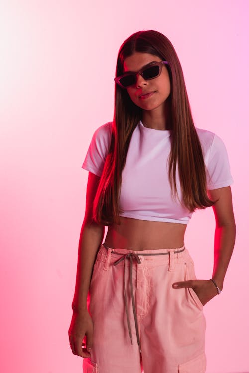 Young Woman in a Crop Top and Sunglasses Posing on Pink Background 