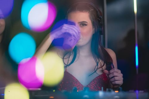 Free A young woman in a red dress with headphones enjoys a vibrant nightlife scene. Stock Photo
