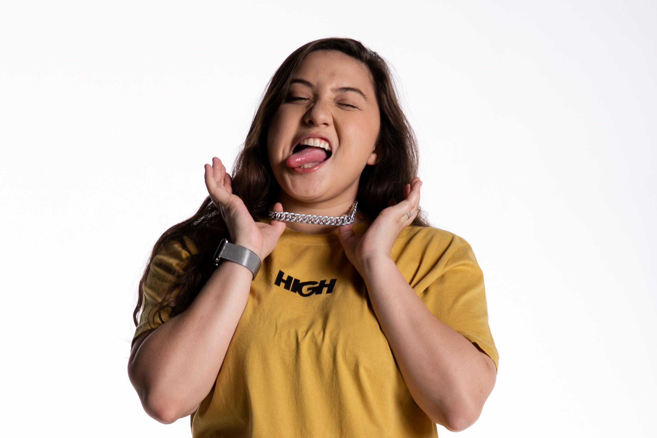 Young woman in yellow t-shirt with a playful expression poses in a studio setting.