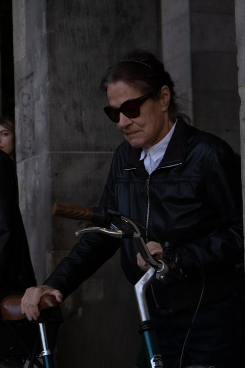 Elderly Woman in Leather Jacket Holding Bike