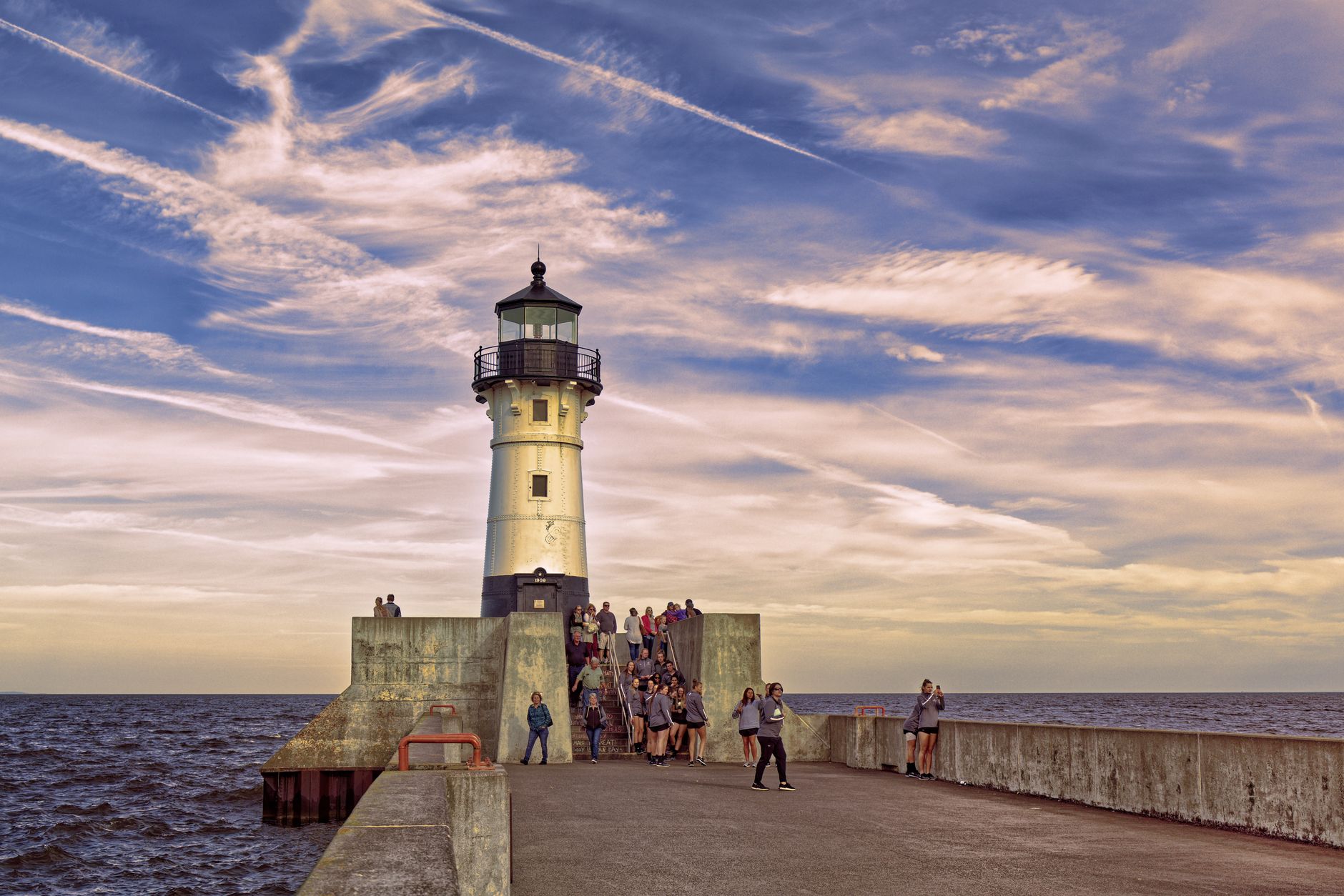 A scenic view of tourists visiting the lighthouse in Duluth, MN, against a beautiful sky.