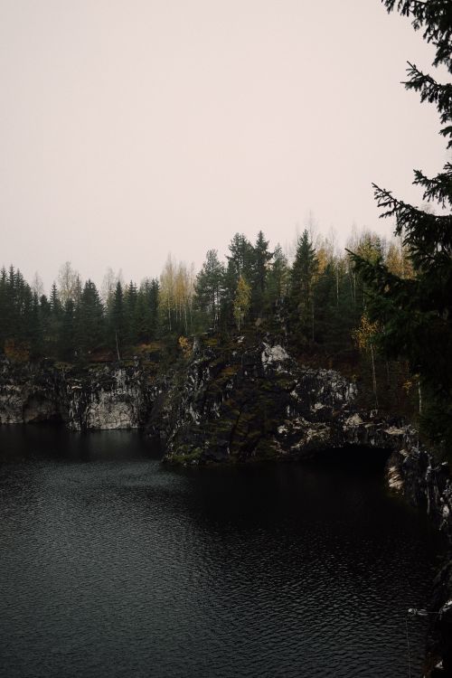 Free A serene autumn forest with rocky cliffs and a misty atmosphere by a dark lake. Stock Photo