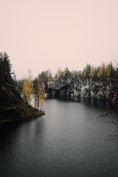 Free Peaceful autumn scene with a lake bordered by rocky cliffs and forested trees. Stock Photo