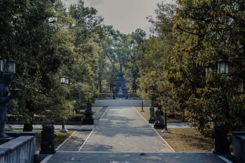 Free Calm pathway surrounded by lush trees, leading to a serene Buddhist statue with intricate stonework. Stock Photo