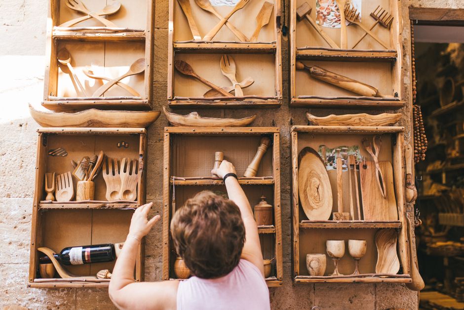 A woman selects a piece from a handmade wooden kitchenware set displayed on rustic shelves.
