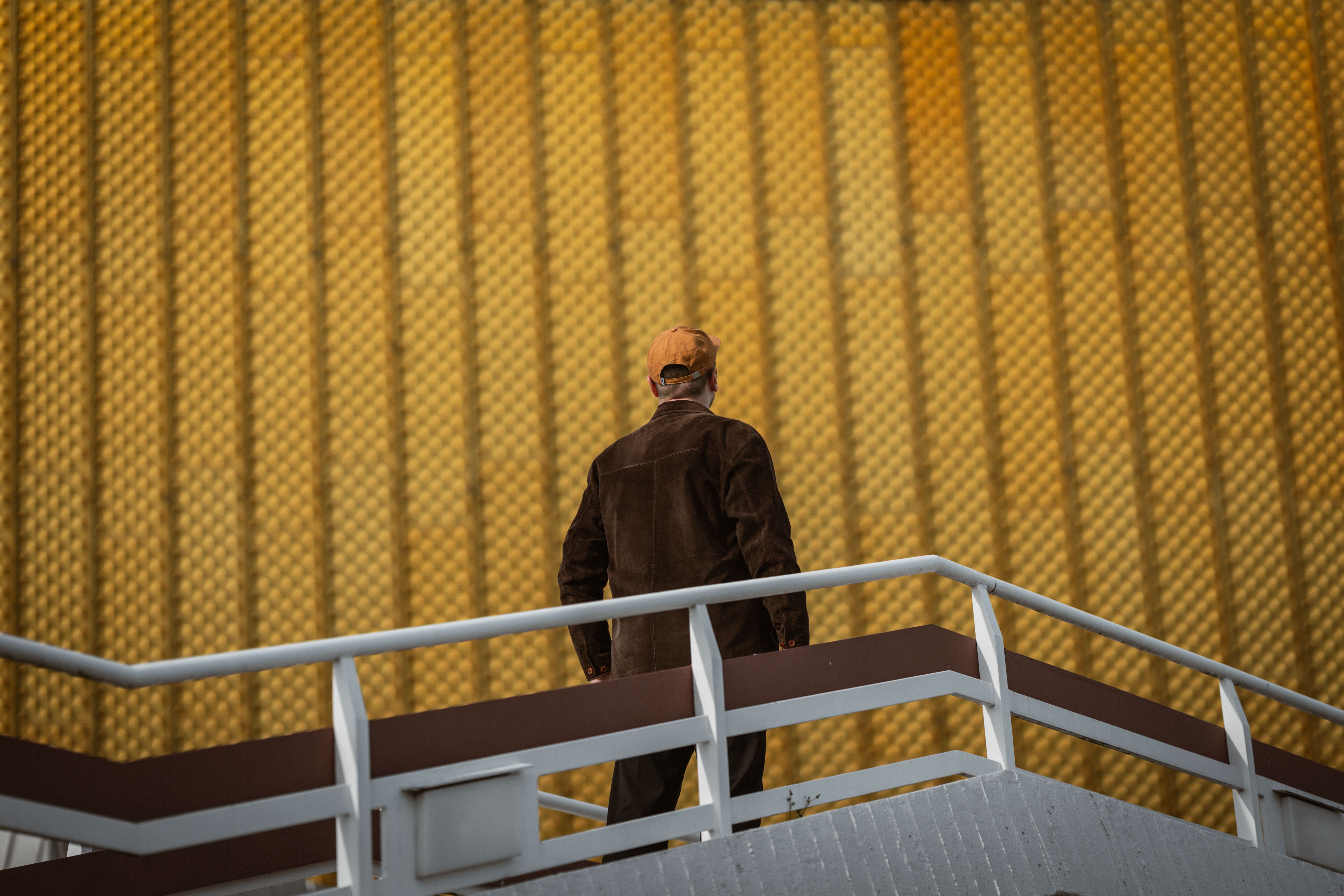 A man stands on a staircase against a striking yellow textured wall, creating a unique visual.