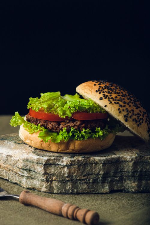 Free Appetizing gourmet burger with fresh lettuce and tomato on a rustic background. Stock Photo