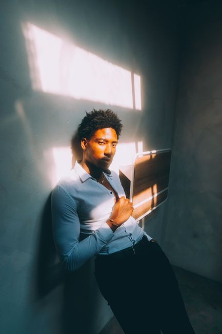 Fashion portrait of a man leaning against a wall in urban Atlanta, showcasing casual style and natural lighting.