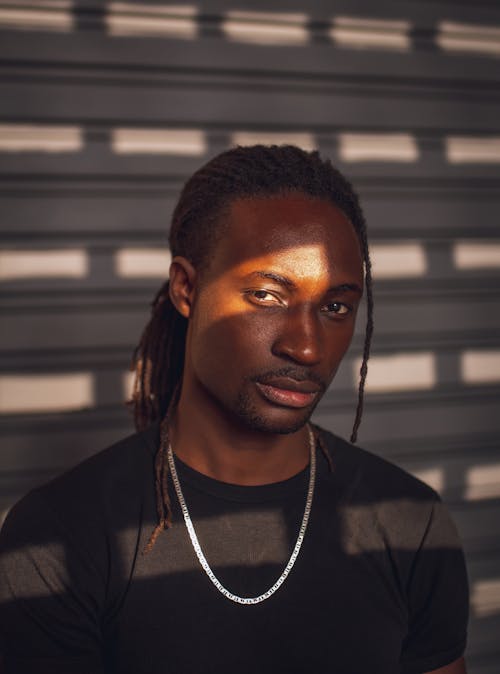 Man Wearing a Black T-shirt and a Necklace Standing in Sunlight 