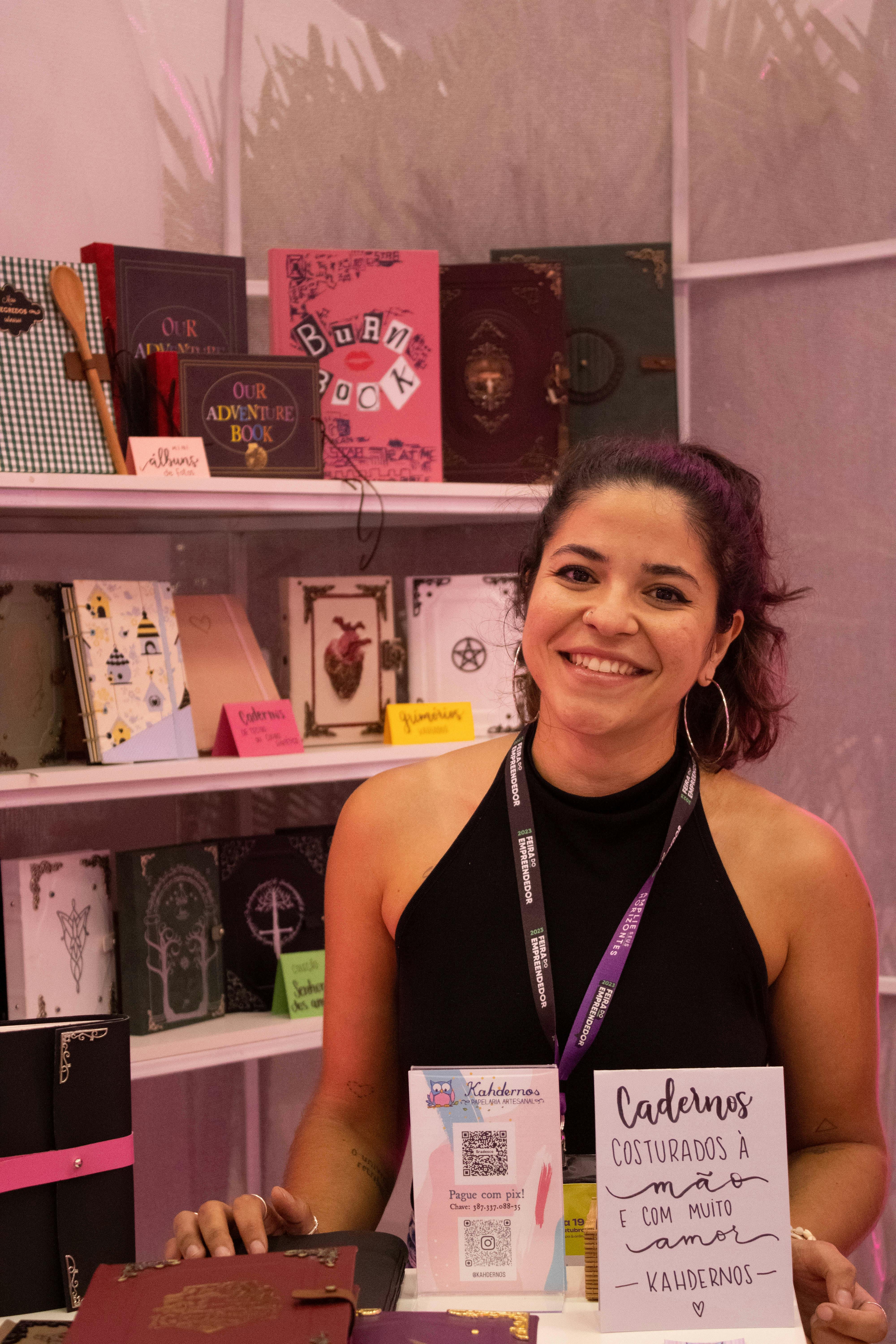 Smiling woman at a stationery booth with a variety of colorful notebooks displayed.