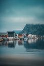 Idyllic fishing village of Reine in Norway, reflecting in calm waters under a misty sky.