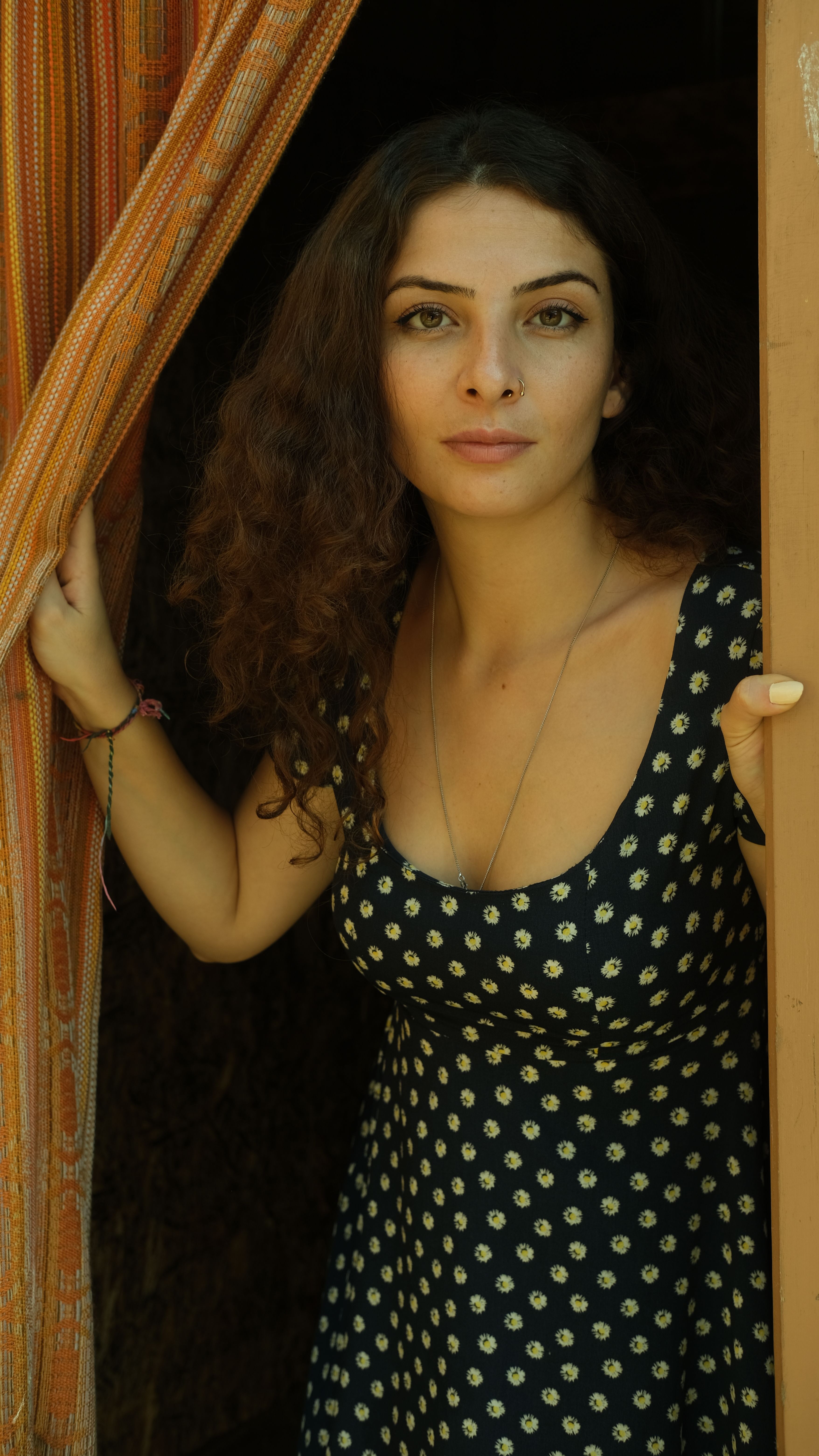 An expressive portrait of a young brunette woman with curly hair, poised at a doorway.