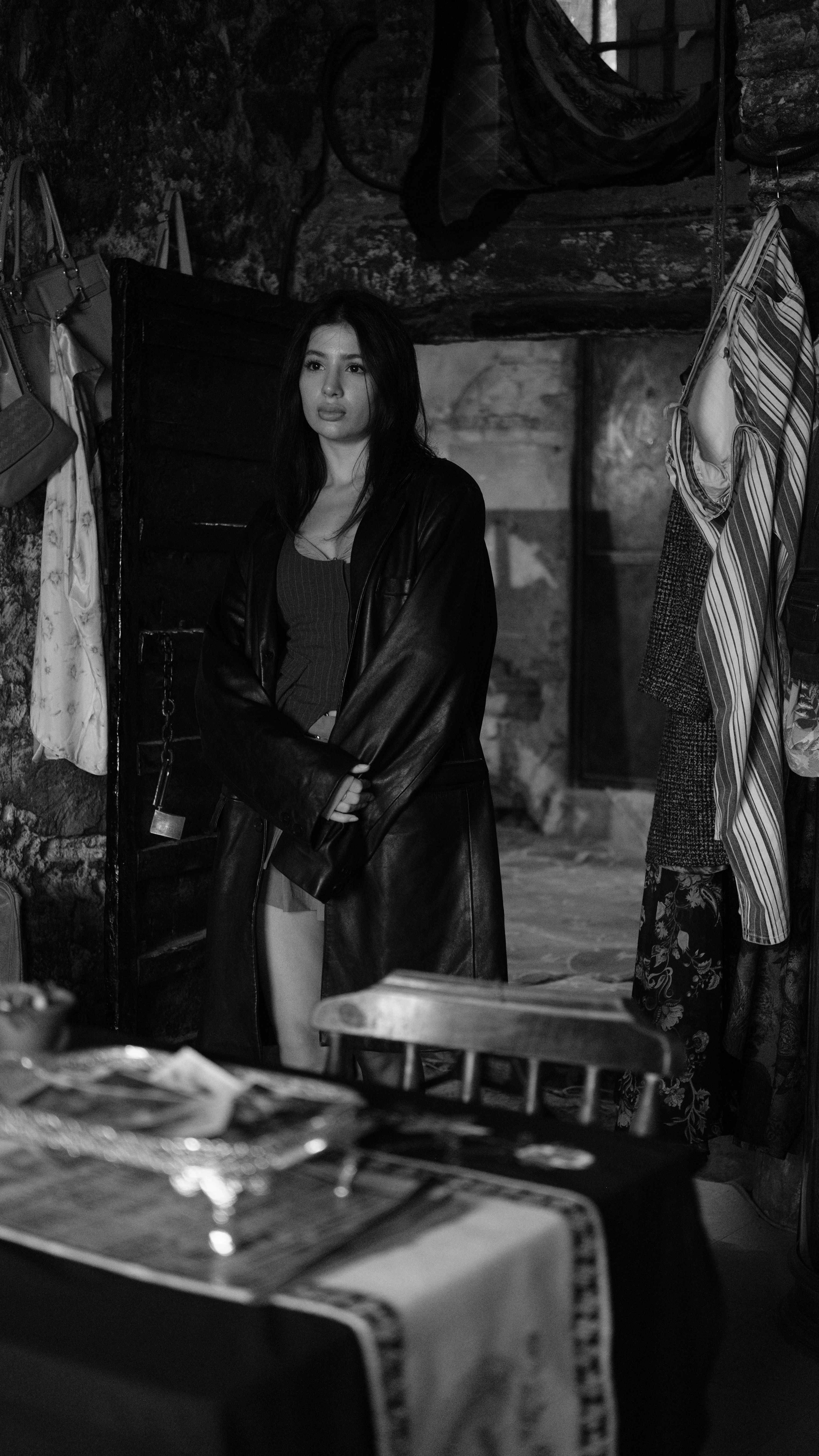 Stylish woman in a coat stands indoors for a dramatic black and white portrait.