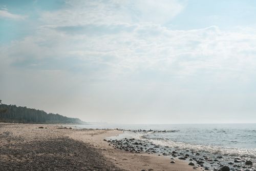 Free Tranquil beach scene with rocks, mist, and a calm ocean under a cloudy sky. Stock Photo