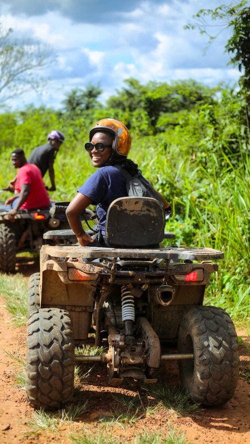 Free Two people enjoying a thrilling quad biking adventure on a dirt road amidst lush greenery. Stock Photo
