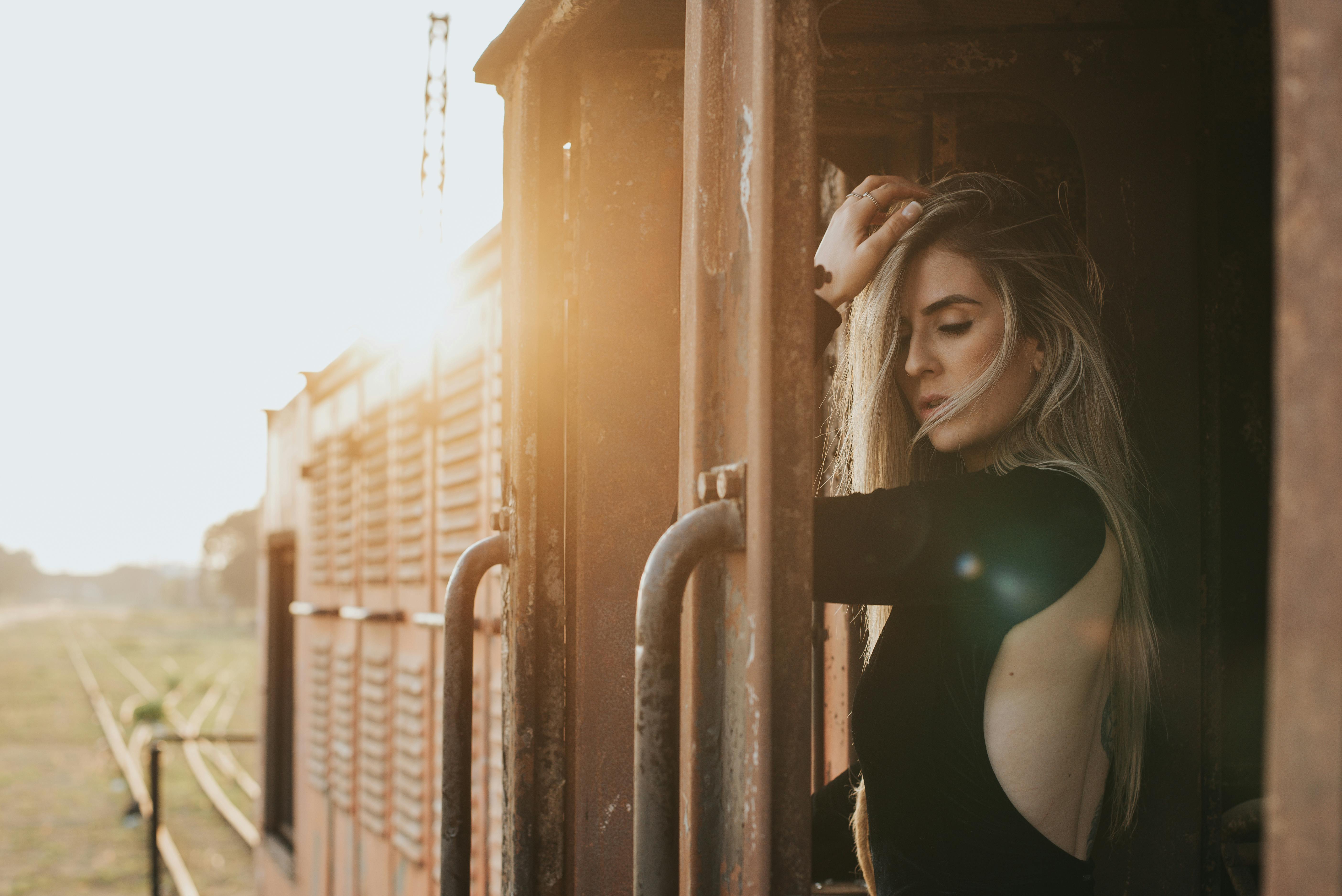 一位身着黑色连衣裙的优雅女子在火车上摆姿势，太阳耀斑让这一幕更加突出