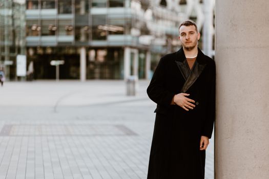 Man in a coat standing against a pillar in Manchester's urban setting.