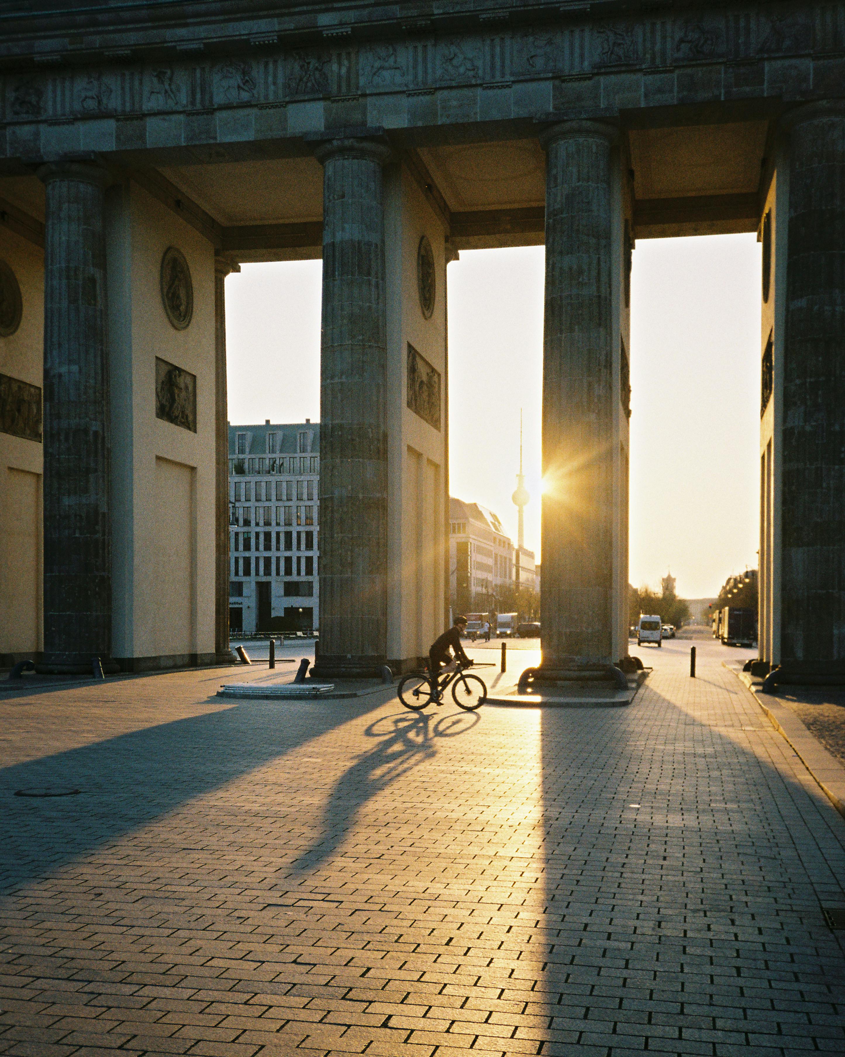 A cyclist passes through Brandenburg Gate in Berlin at sunset.