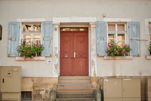 Free Charming old building featuring a rustic door and pastel wooden shutters adorned with flowers. Stock Photo