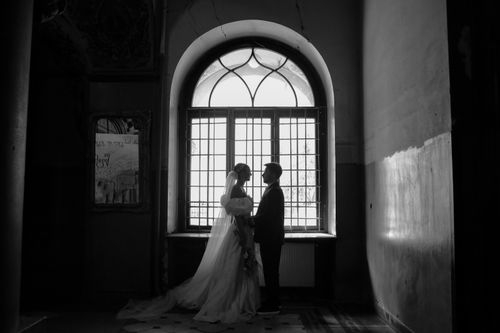 Free Elegant black and white portrait of a newlywed couple standing by a window. Stock Photo