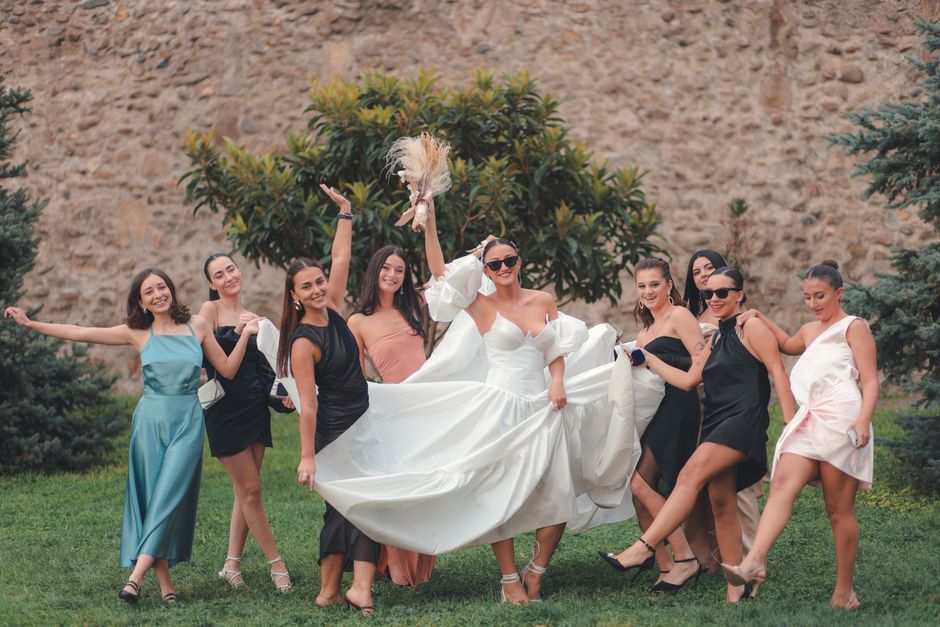 Joyful bride and bridesmaids pose cheerfully in elegant dresses outside.