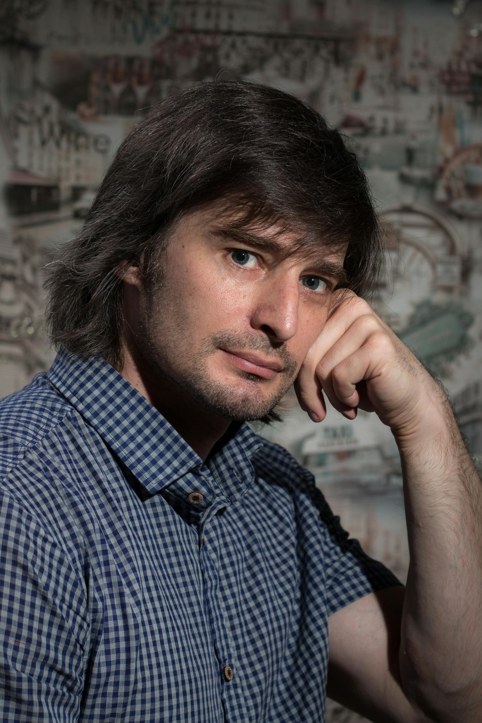 A thoughtful man in a checkered shirt poses indoors, exuding a serene and pensive vibe.