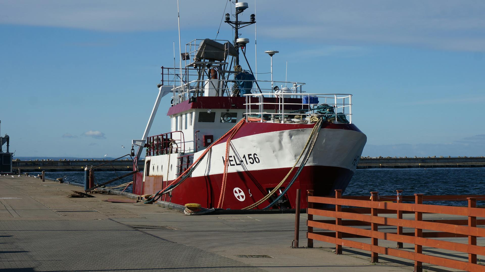 A fishing vessel moored at a sunny harbor, showcasing nautical ropes and a clear blue sky.