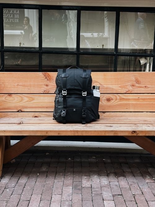 Free Stylish black backpack resting on a wooden bench outdoors in Amsterdam. Stock Photo