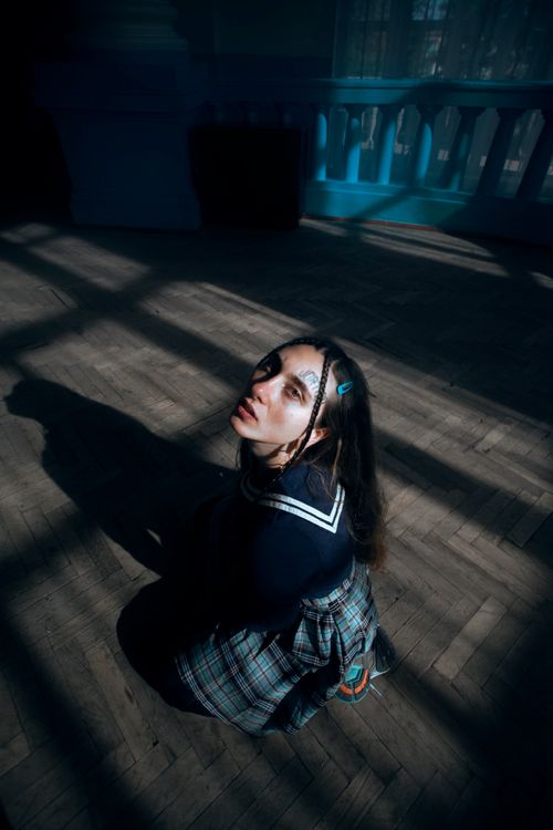 Free A young woman wearing a plaid skirt sits dramatically in sunlight with shadows indoors. Stock Photo