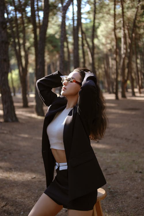 A woman in a black jacket and skirt posing in the woods