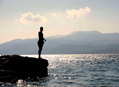 Person Standing on Rock Besides Sea Near Island during Daytime