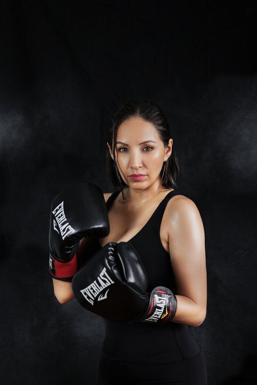 Free Portrait of a determined female boxer wearing gloves, striking a pose indoors. Stock Photo