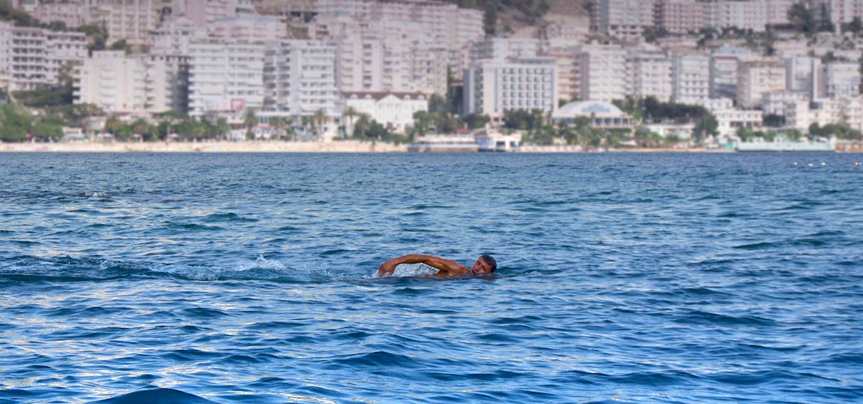 grátis Homem Nadando Em Um Corpo D'água Prédio Alto De Concreto Branco No Fundo Foto profissional