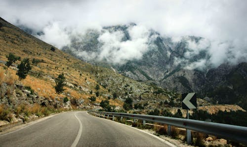 Concrete Road Near Cliff and Hill during Daytime