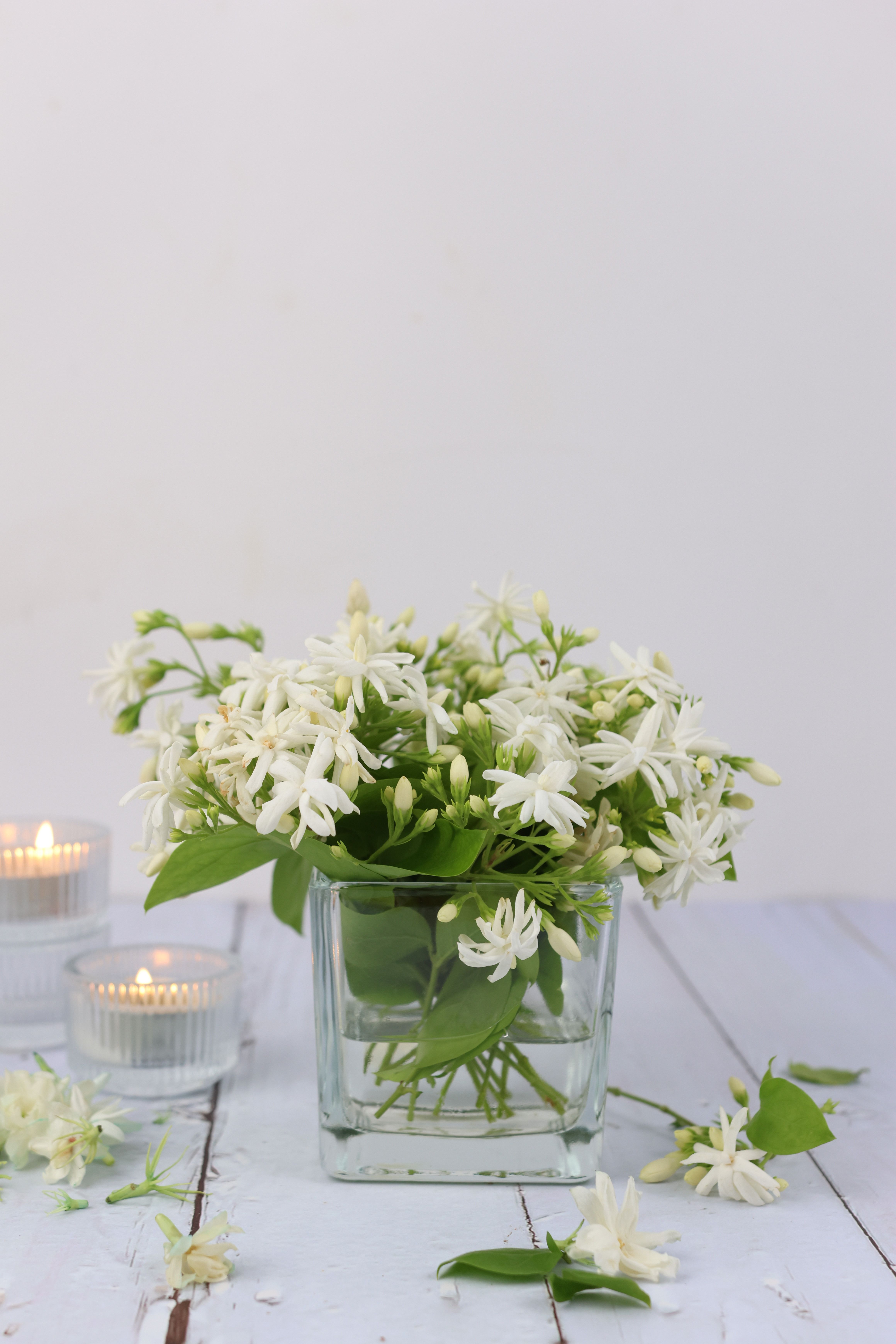 Elegant white jasmine arrangement in glass vase with candles on rustic surface.