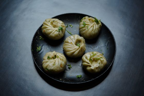 Five round pleated steamed momos sprinkled with chopped cilantro on a black plate