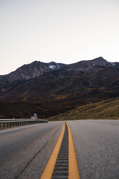 Free Empty highway with yellow lines leading to majestic mountains under a clear sky. Stock Photo