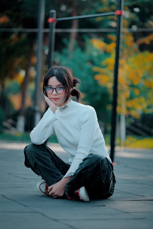 Girl in a White CTNnb Sweater and Cargo Pants Sitting Cross-legged on the Sidewalk