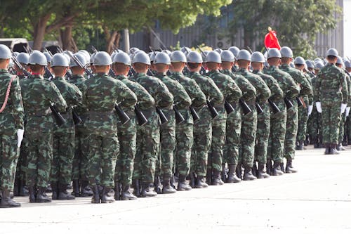 Back view unrecognizable soldiers with riffles wearing khaki uniform and hardhat lining up in rows during military ceremony