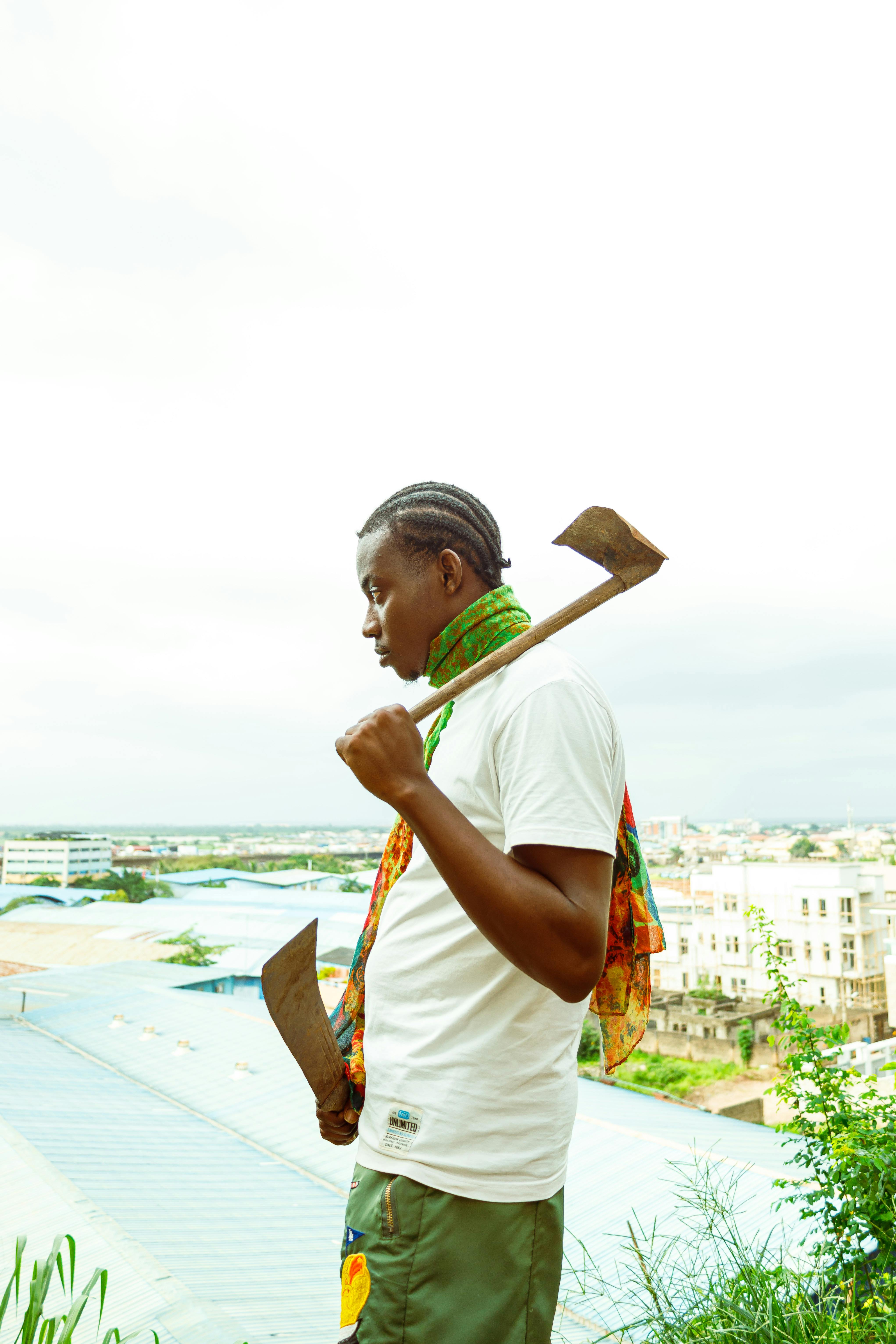 Young man in urban setting holding an axe and looking thoughtful.