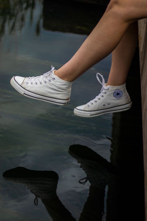 Free Close-up of legs and white sneakers reflecting in water, capturing relaxation outdoors. Stock Photo