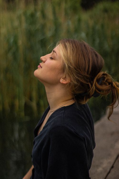 Free A woman peacefully meditating by a lakeside, enjoying nature's tranquility. Stock Photo