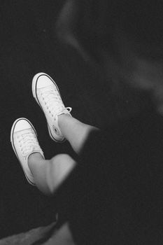 Stylish black and white shot focusing on white sneakers worn by a woman.