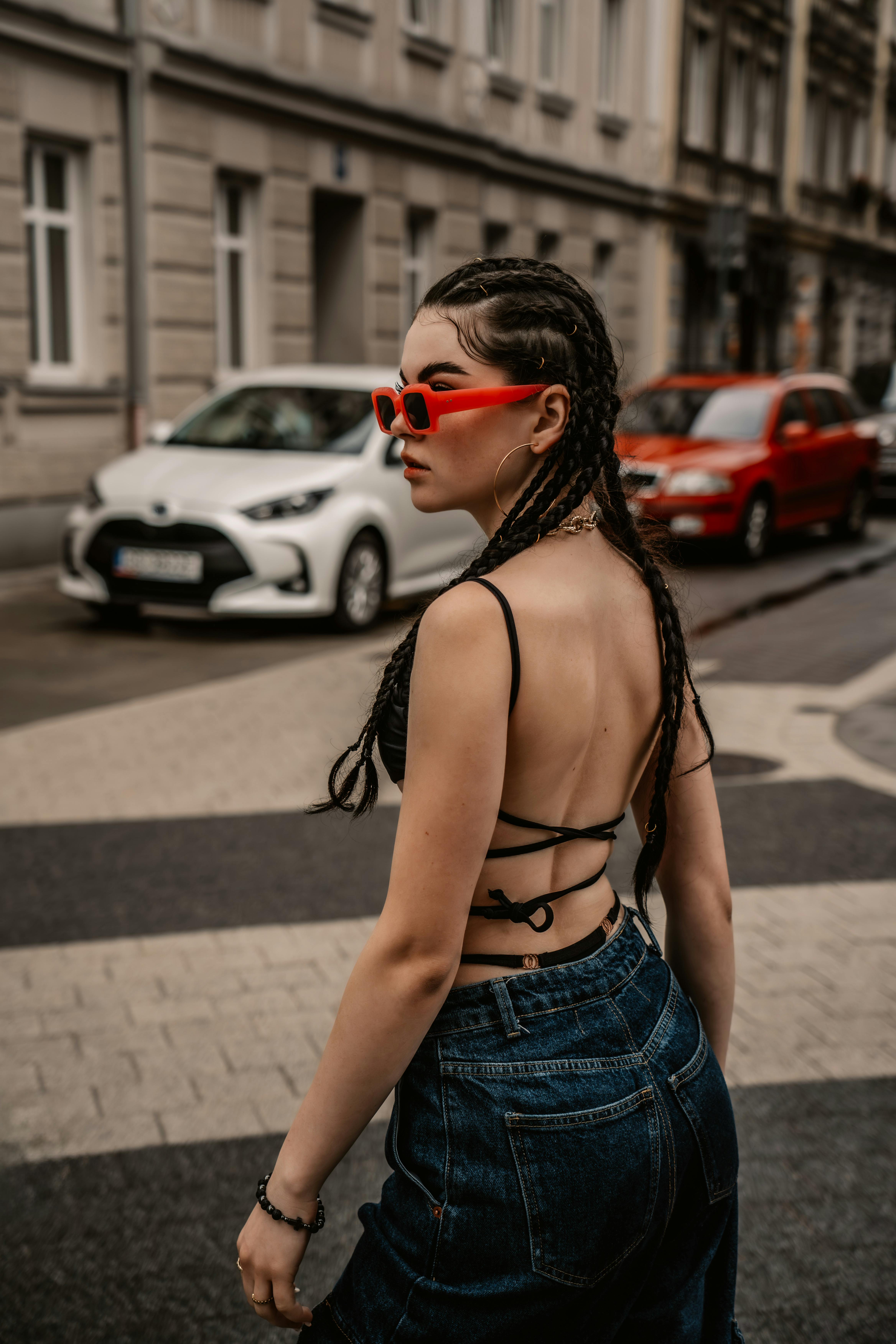 Stylish woman in halterneck top and braided hair crossing a city street.